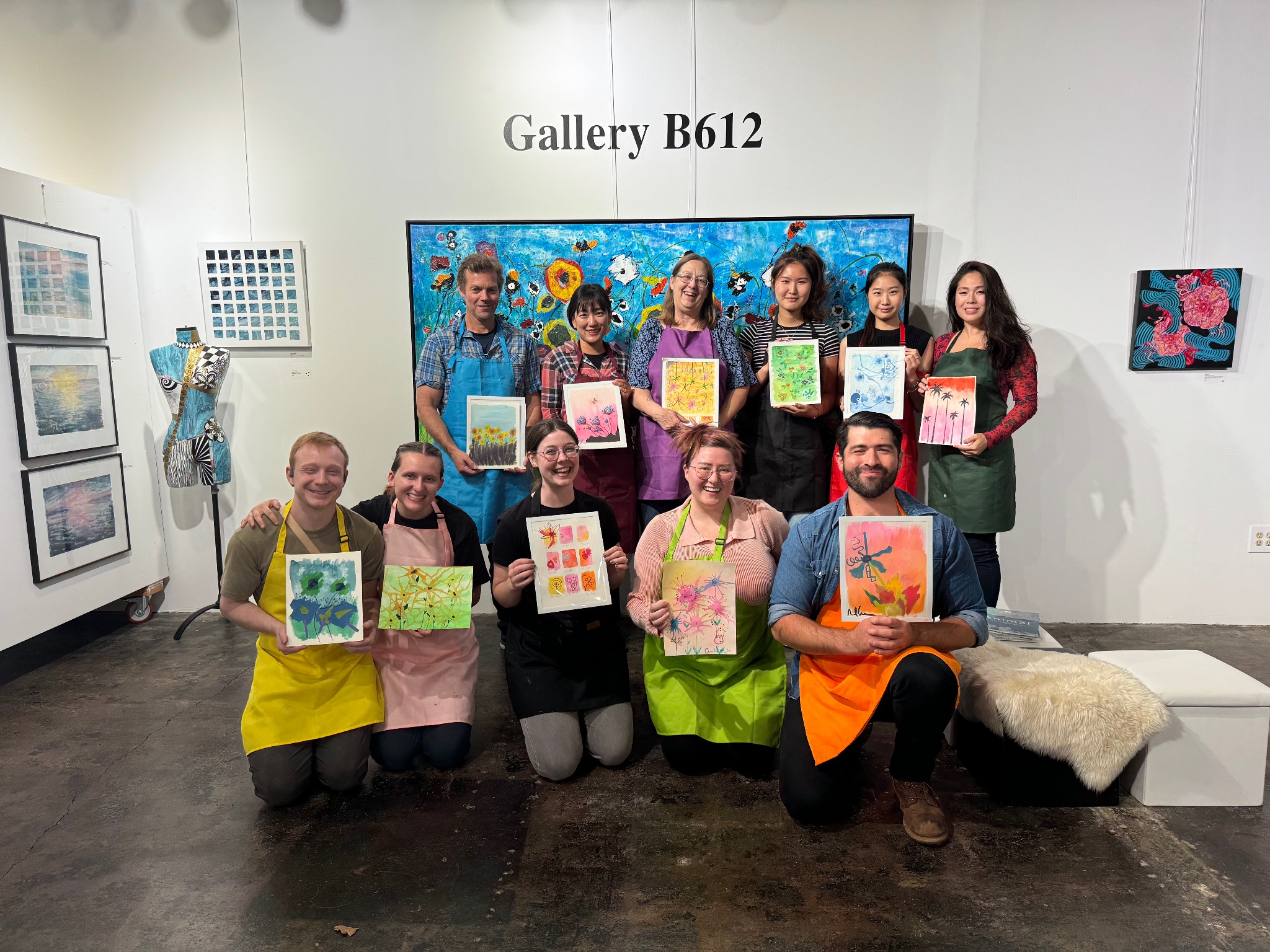 Participants holding completed artworks inside Gallery B612 after a community art workshop.